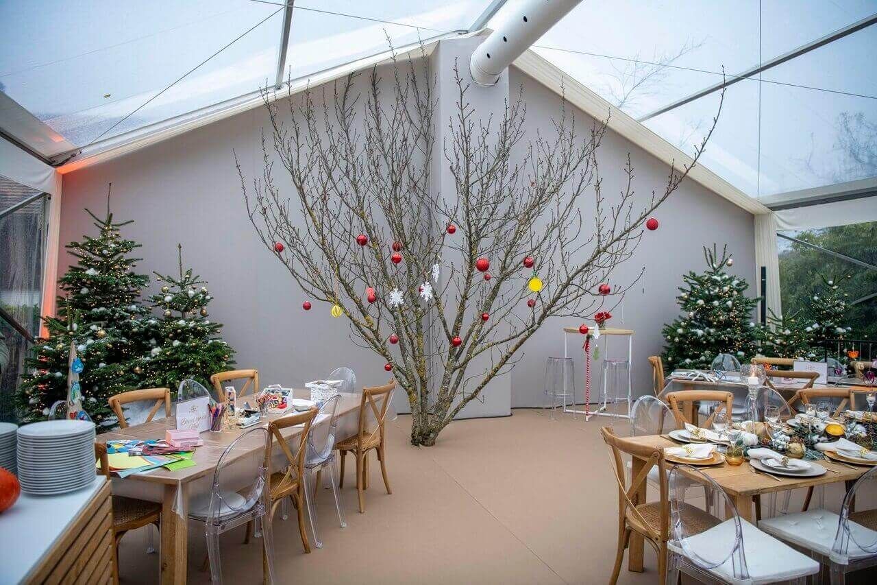 Espace repas extérieur festif avec tables décorées et un grand arbre sous une canopée blanche