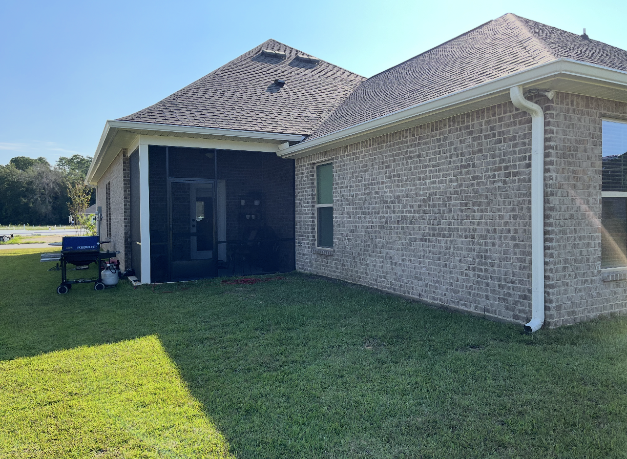 Exterior view of a brick house with a screened-in patio and green lawn on a sunny day.