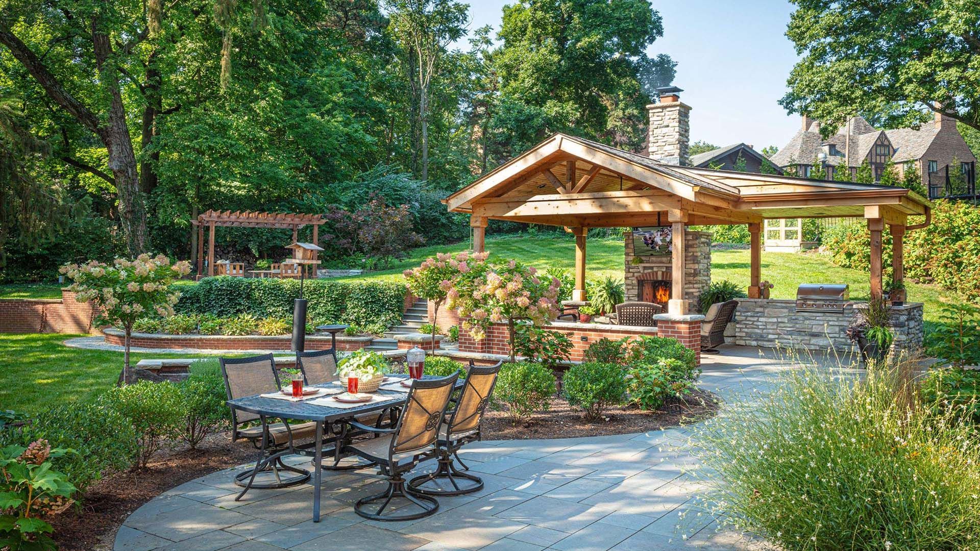 Patio with table, chairs, outdoor fireplace, and pergola in a lush green garden.
