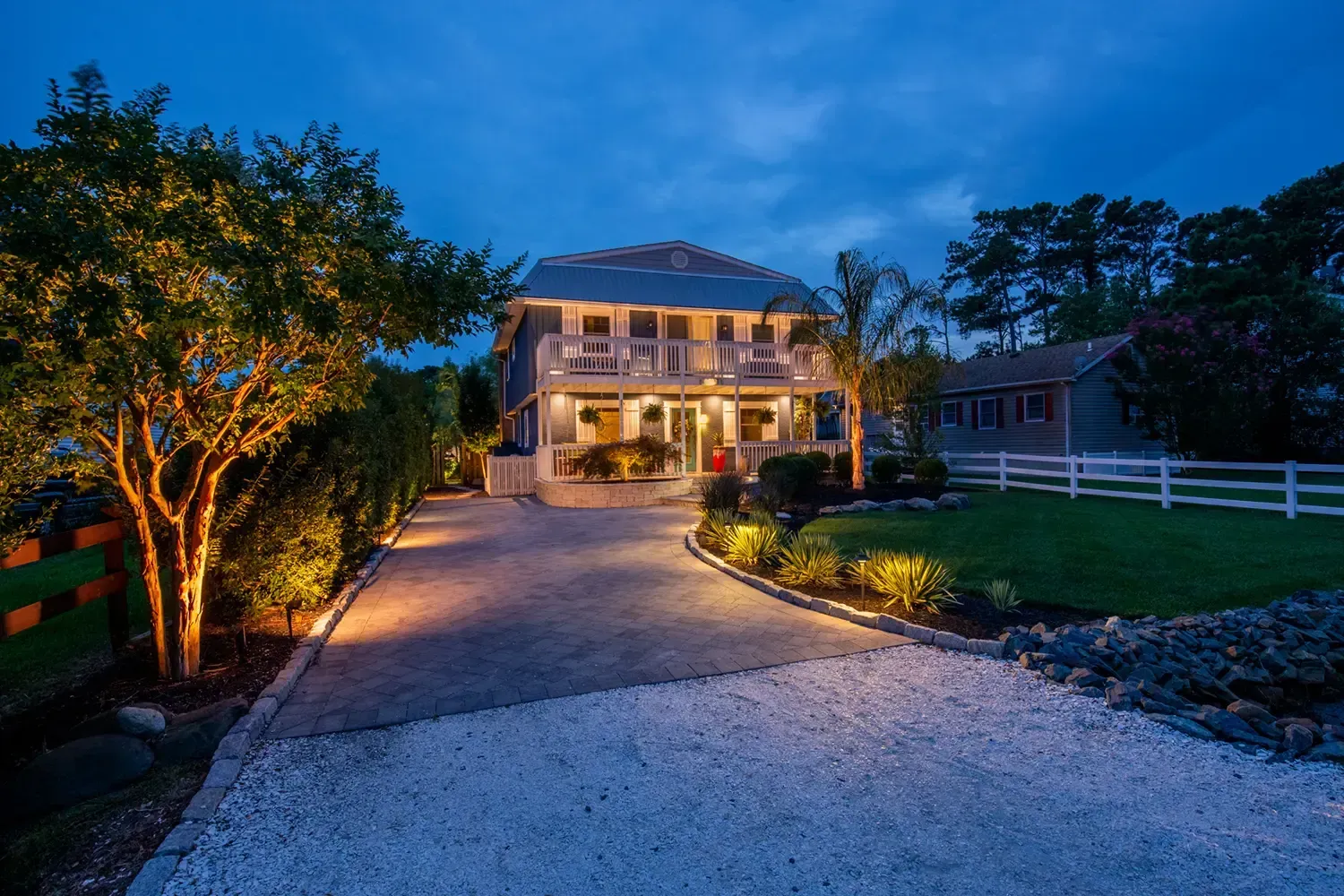 Night view of a two-story house with outdoor lighting on a gravel driveway.