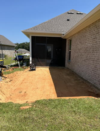 Backyard patio under construction with screen enclosure, house, and red dirt.