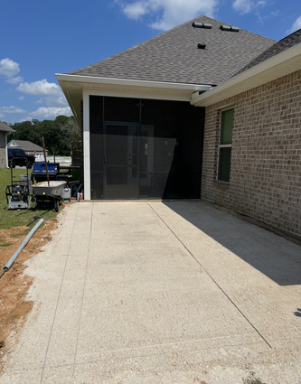 Concrete patio next to a brick house with a screened-in porch. Construction materials are visible.