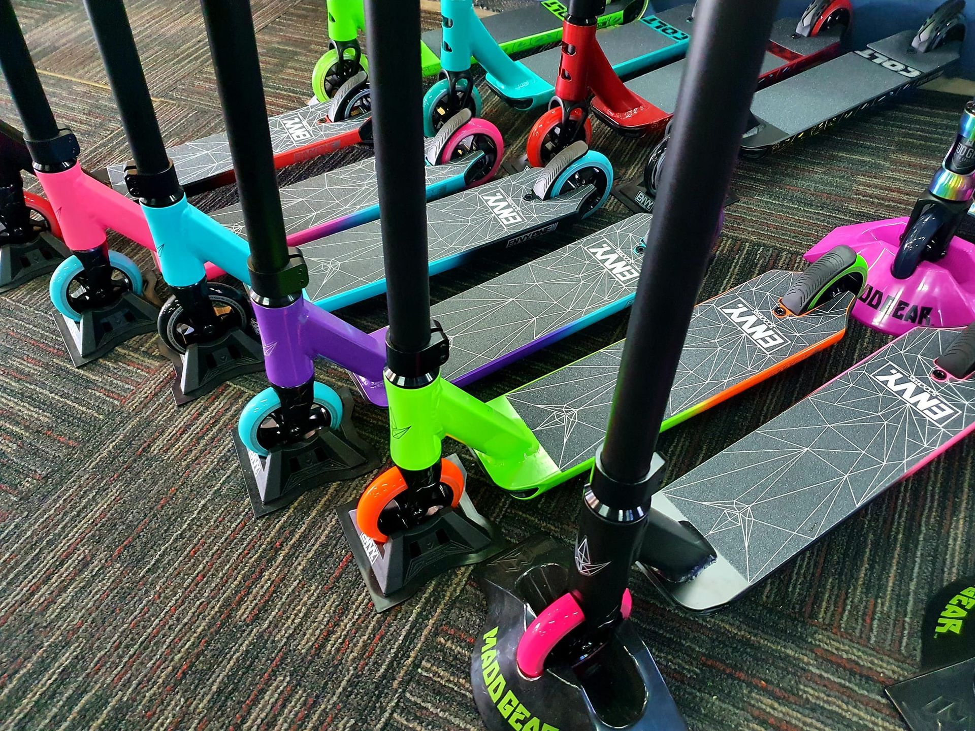 Row of colourful scooters with black handlebars on patterned carpet — City Centre Cycles in Berserker, QLD