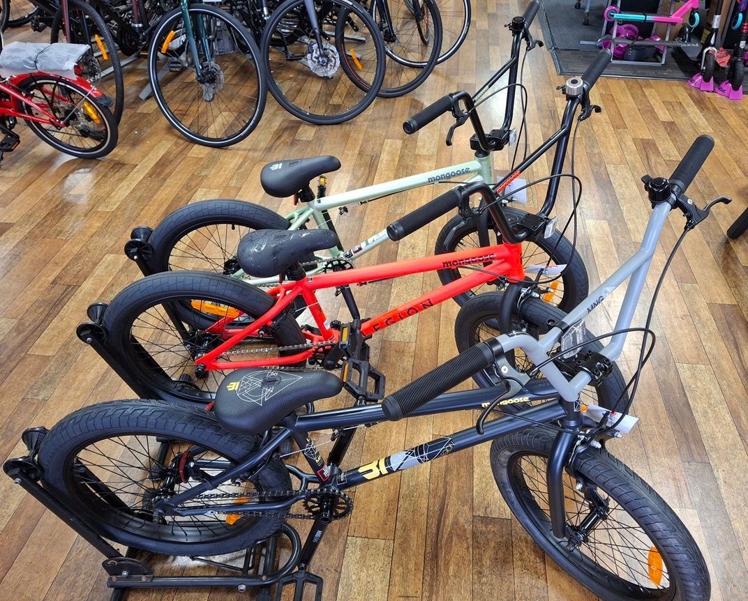 Several BMX Bikes in Red, Black, and Grey Arranged on A Wooden Floor Indoors — City Centre Cycles in Berserker, QLD