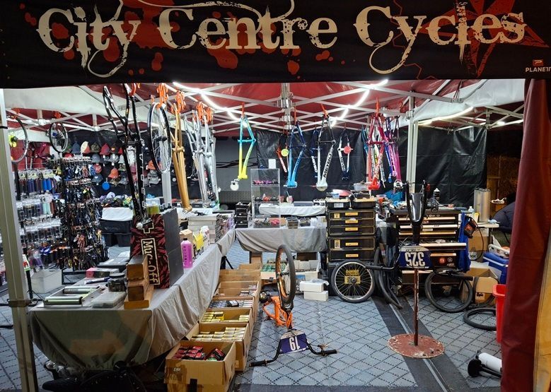 Street market bicycle repair stall with hanging bike parts, tools, and a City Centre Cycles sign — City Centre Cycles in Berserker, QLD