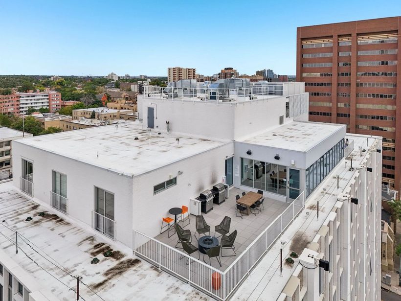 Rooftop patio with table, chairs, grill, and city views from a white building.