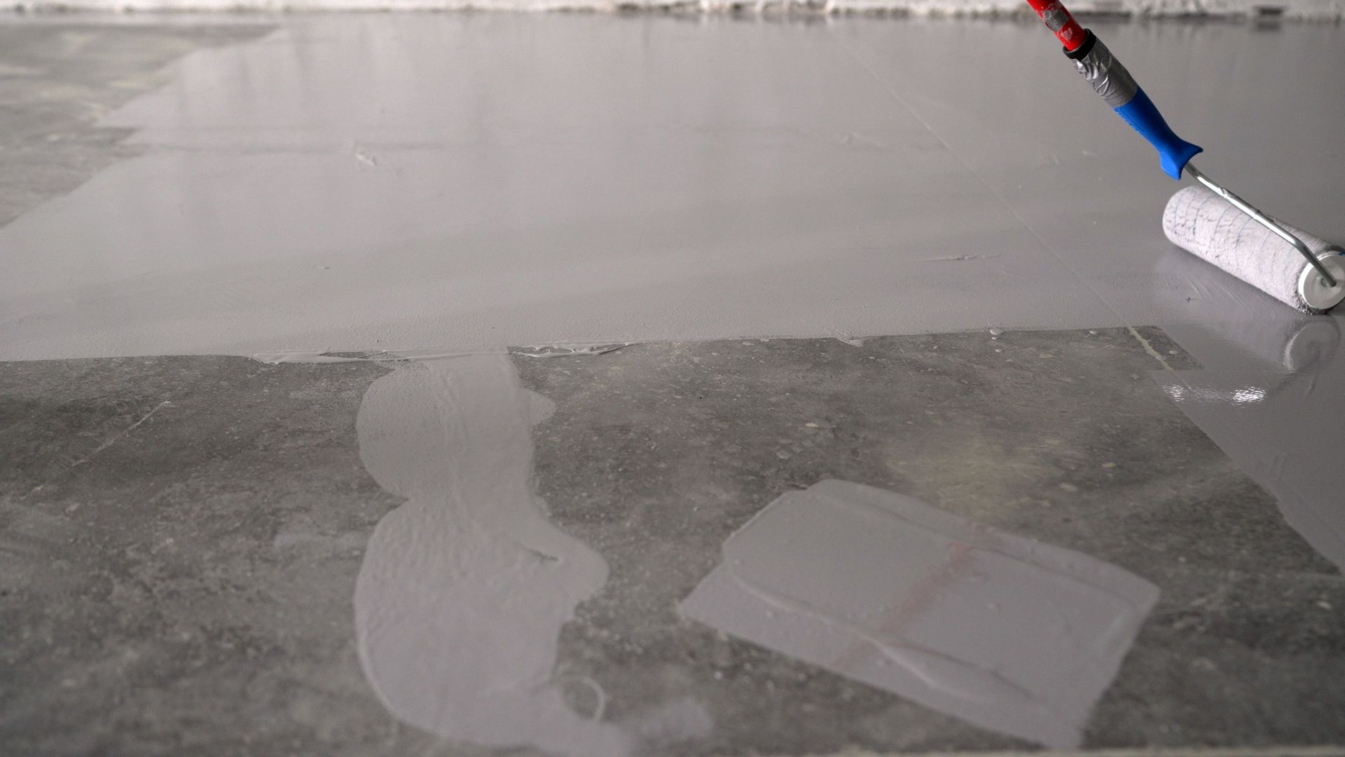 A person rolling gray paint on a floor, with paint roller in hand.