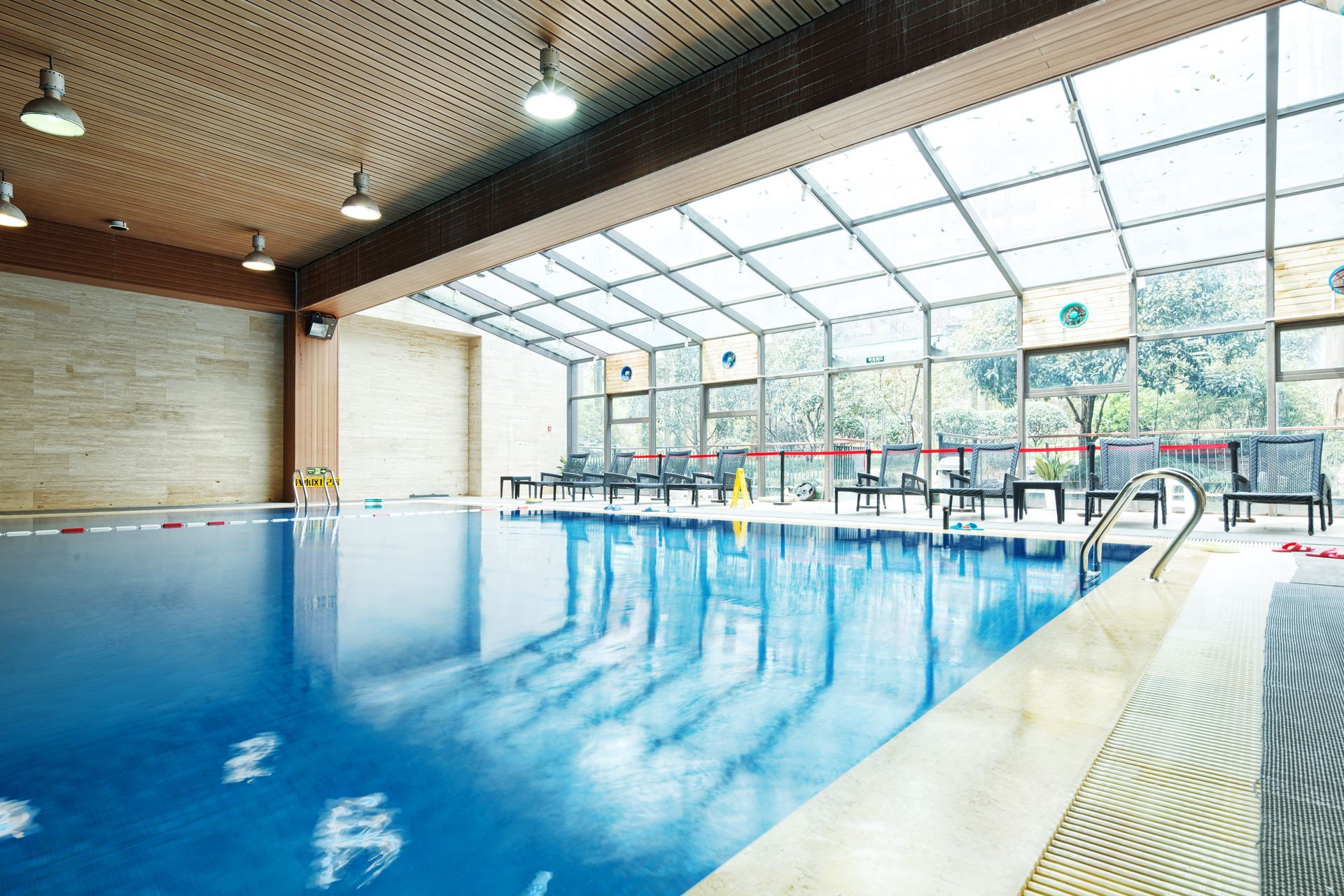 Indoor swimming pool with blue water and glass roof. Lounge chairs line the edge.