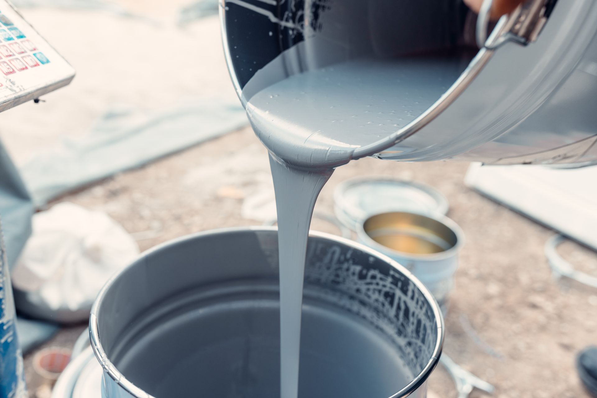 Pouring gray paint from a metal bucket into another. A color palette sits nearby.
