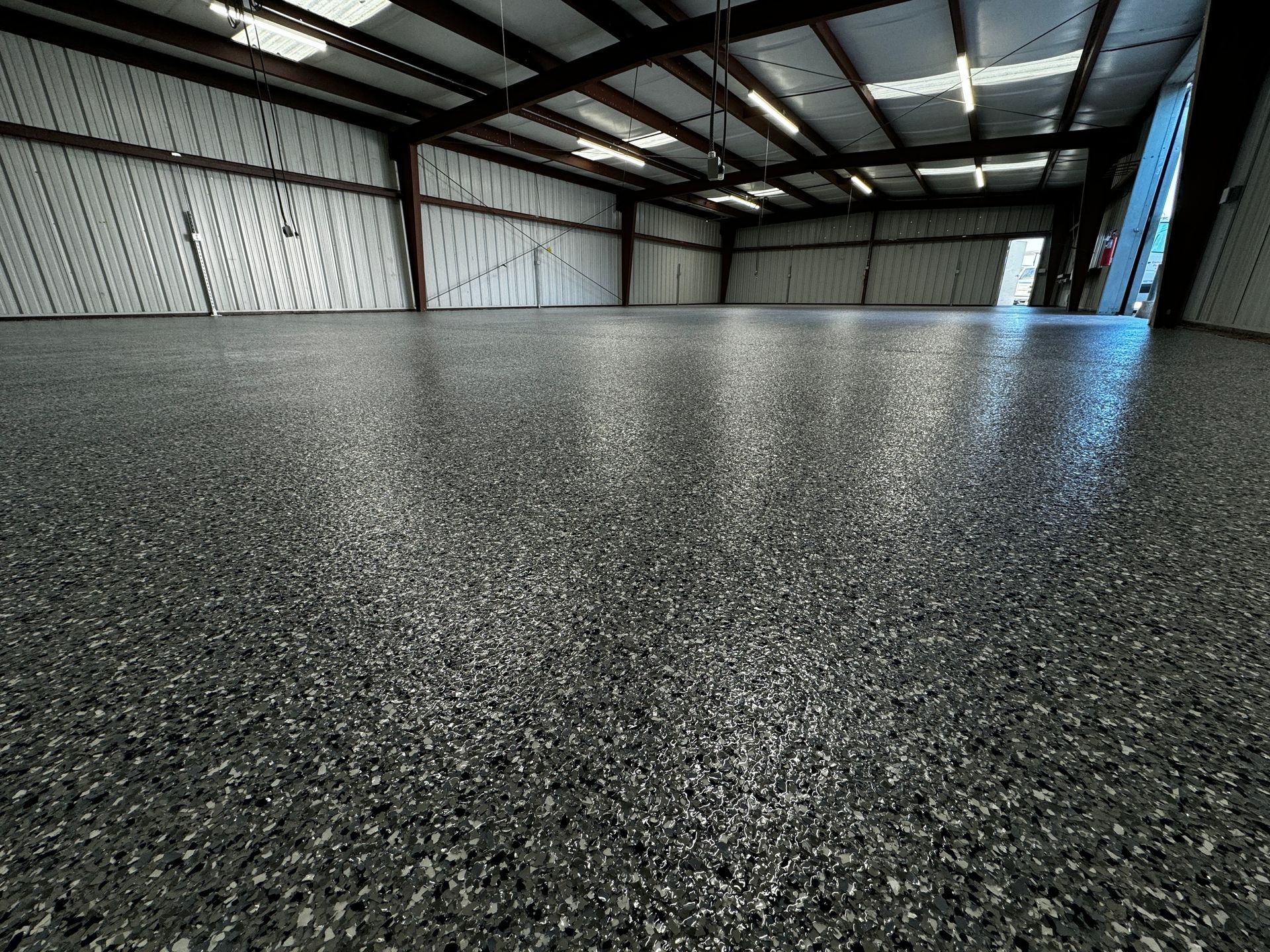 Empty industrial warehouse with a shiny black epoxy floor and metal roof beams