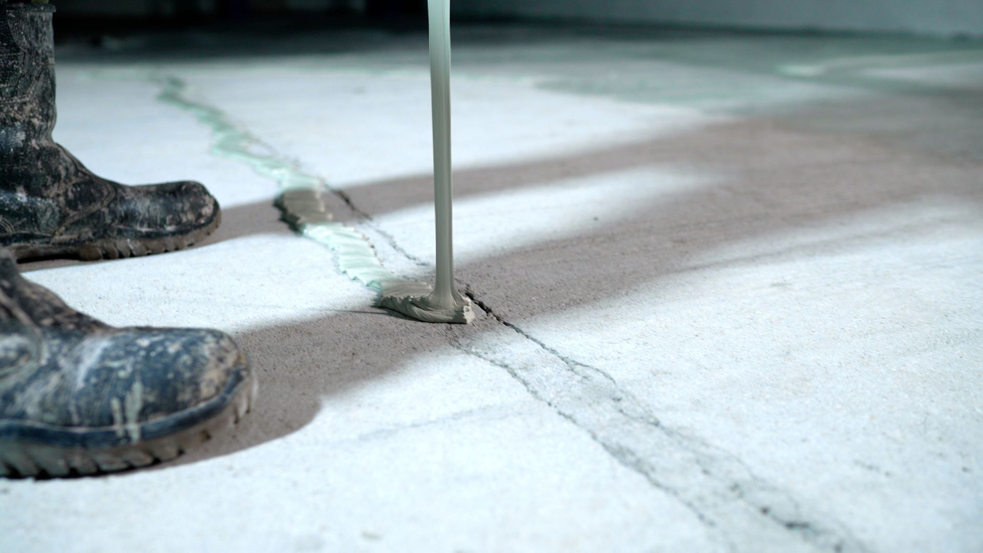 Person in rubber boots pouring sealant into a crack in a concrete floor. Person in rubber boots pouring sealant into a crack in a concrete floor.
