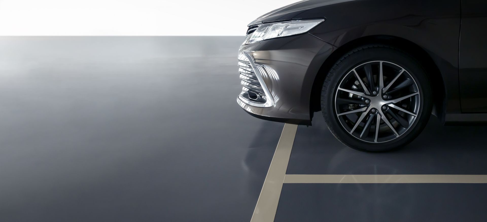 Front corner of a dark gray car parked over a yellow line in a parking garage.
