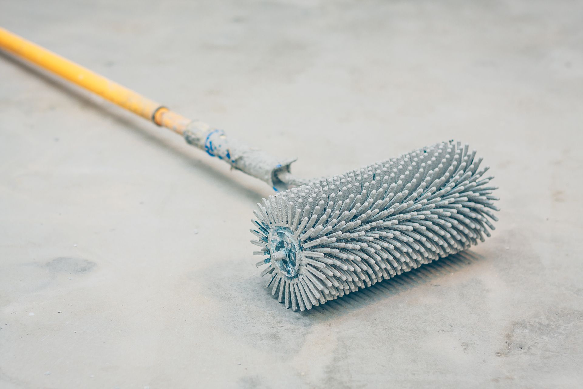 Gray spiked roller tool on a concrete surface with a wooden handle. Gray spiked roller tool on a concrete surface with a wooden handle.