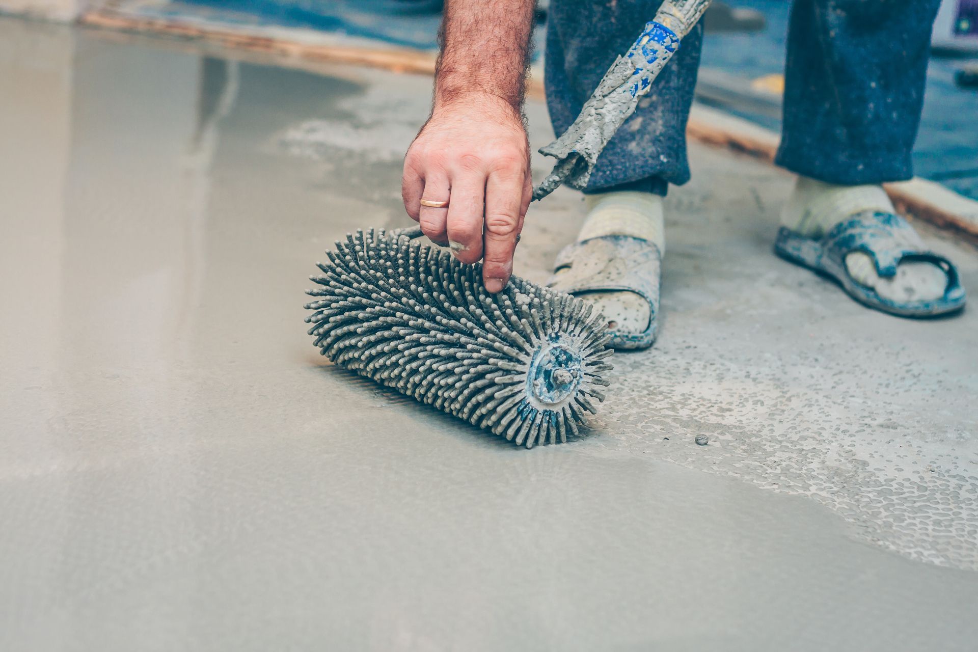 Person using a spiked roller on a gray concrete floor. Person using a spiked roller on a gray concrete floor.