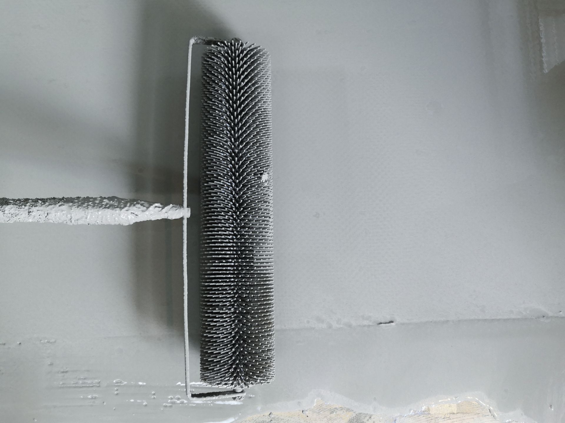 A spiked roller tool is used to remove air bubbles from a freshly applied grey coating on a wall. A spiked roller tool is used to remove air bubbles from a freshly applied grey coating on a wall.