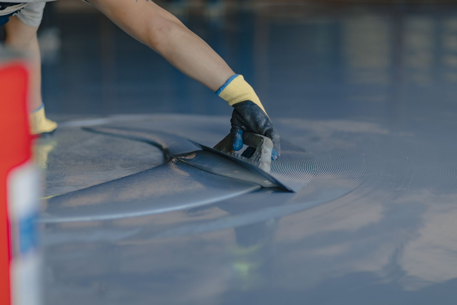 Person smoothing blue epoxy flooring with a trowel, wearing gloves.