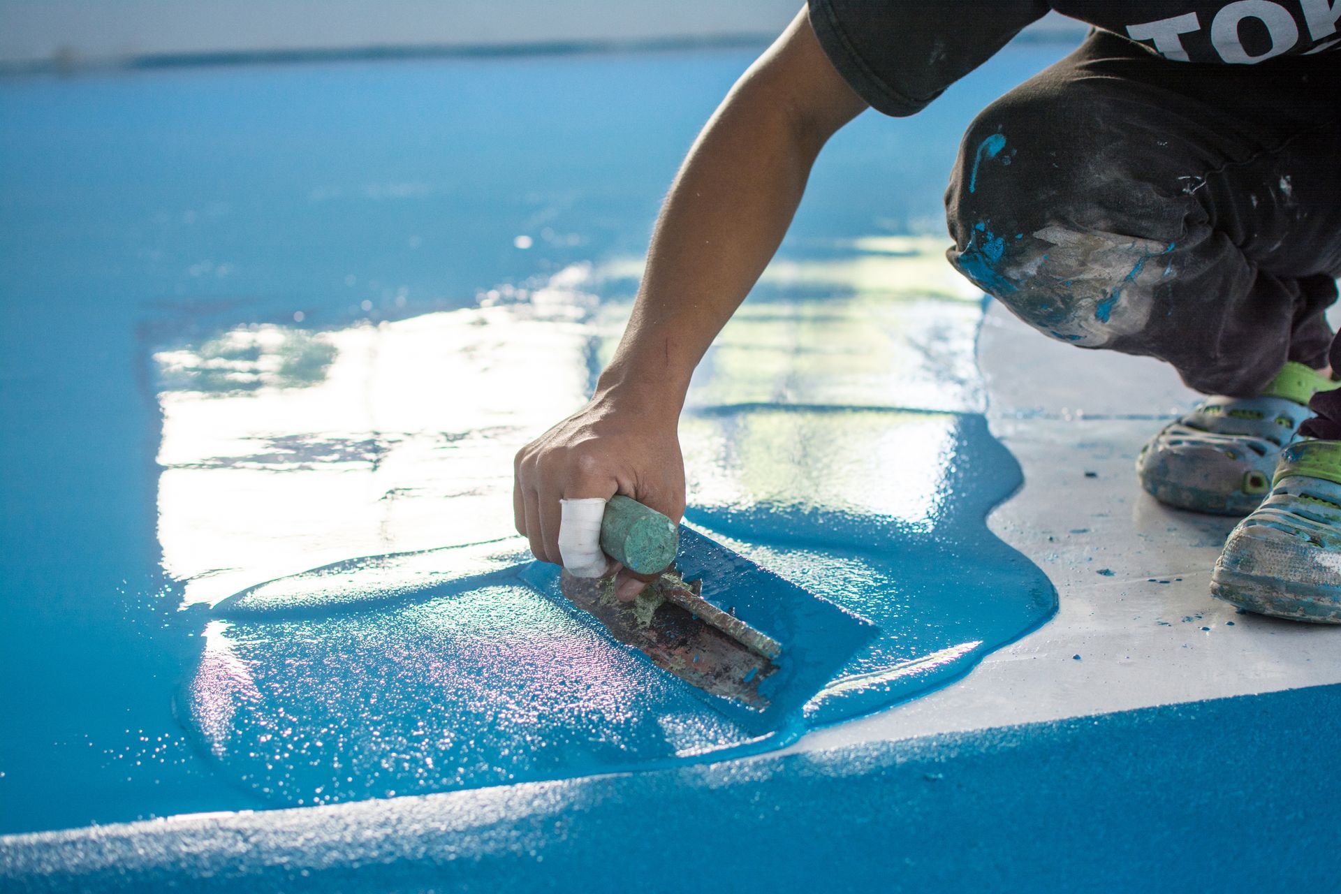 Person applying blue epoxy to a floor with a trowel.