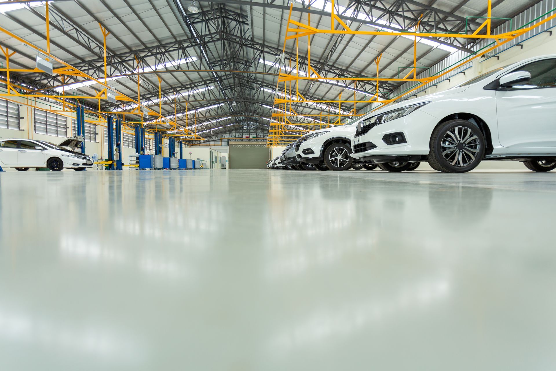 A light-colored, spacious auto repair shop with white cars parked on a shiny gray floor. A light-colored, spacious auto repair shop with white cars parked on a shiny gray floor.