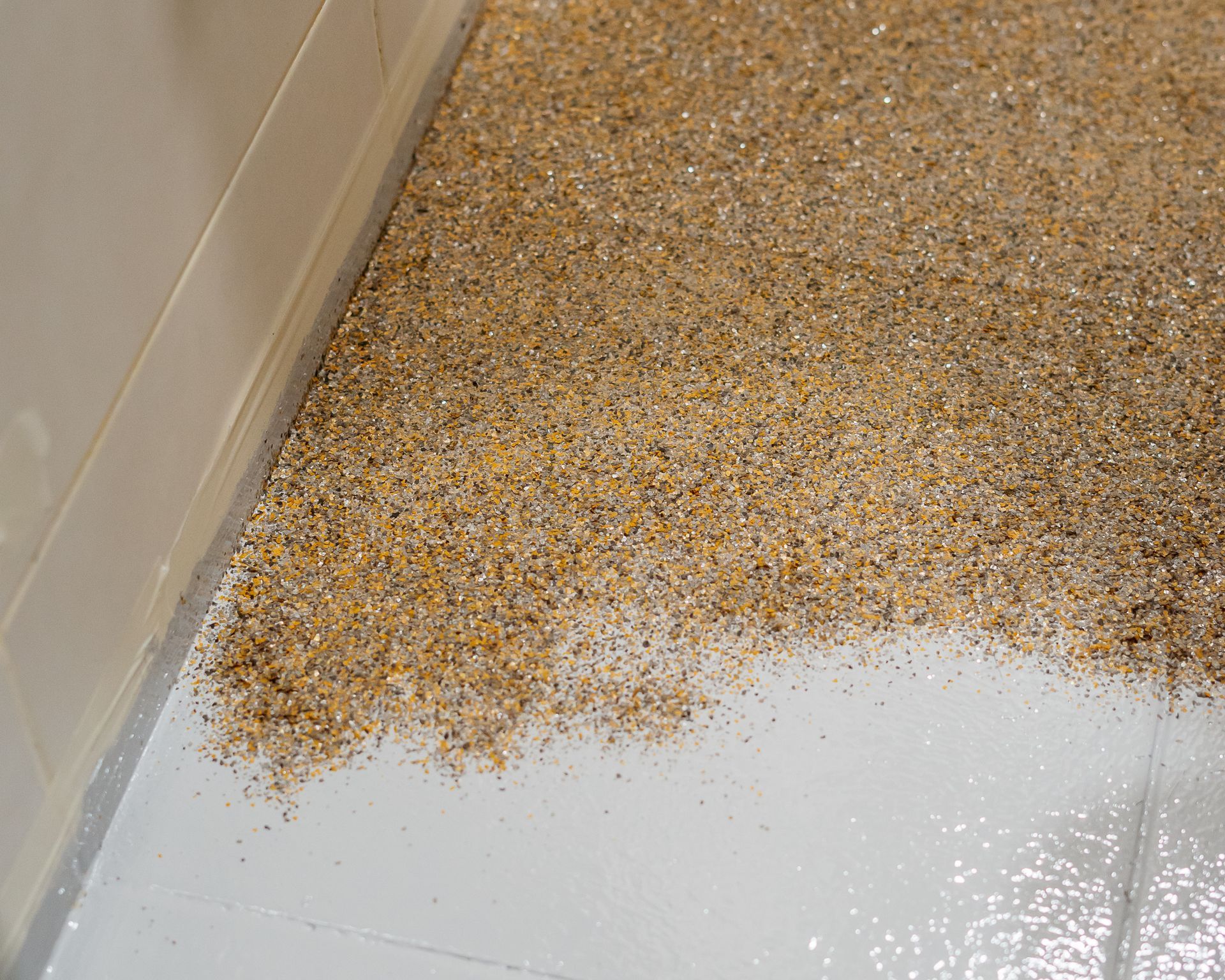 Gravelly, beige surface covering a floor next to a white wall. Gravelly, beige surface covering a floor next to a white wall.