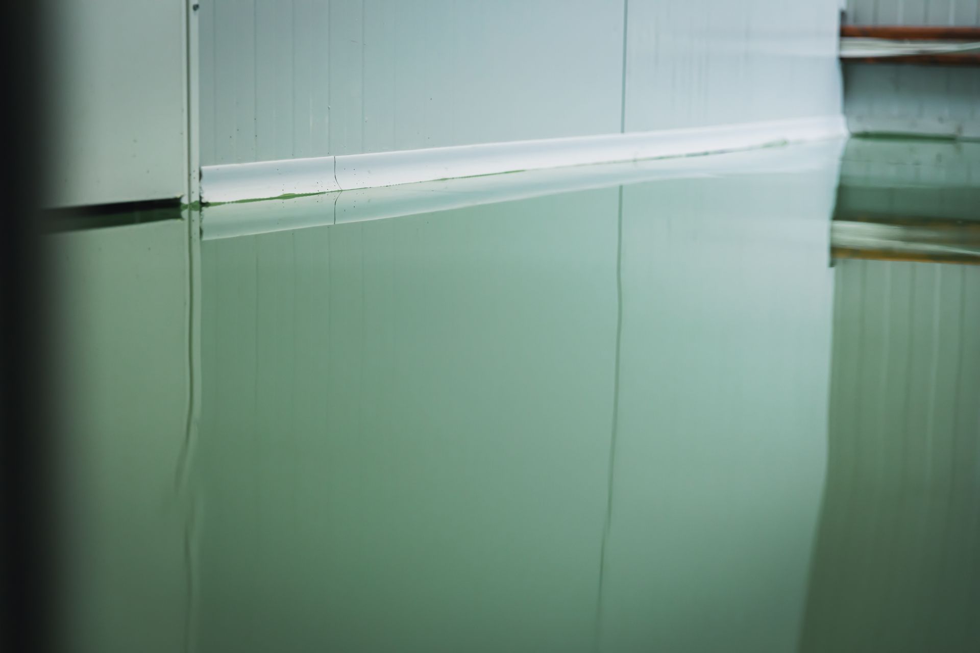 Reflective, green-toned epoxy floor with a light-colored wall reflected in it. Reflective, green-toned epoxy floor with a light-colored wall reflected in it.
