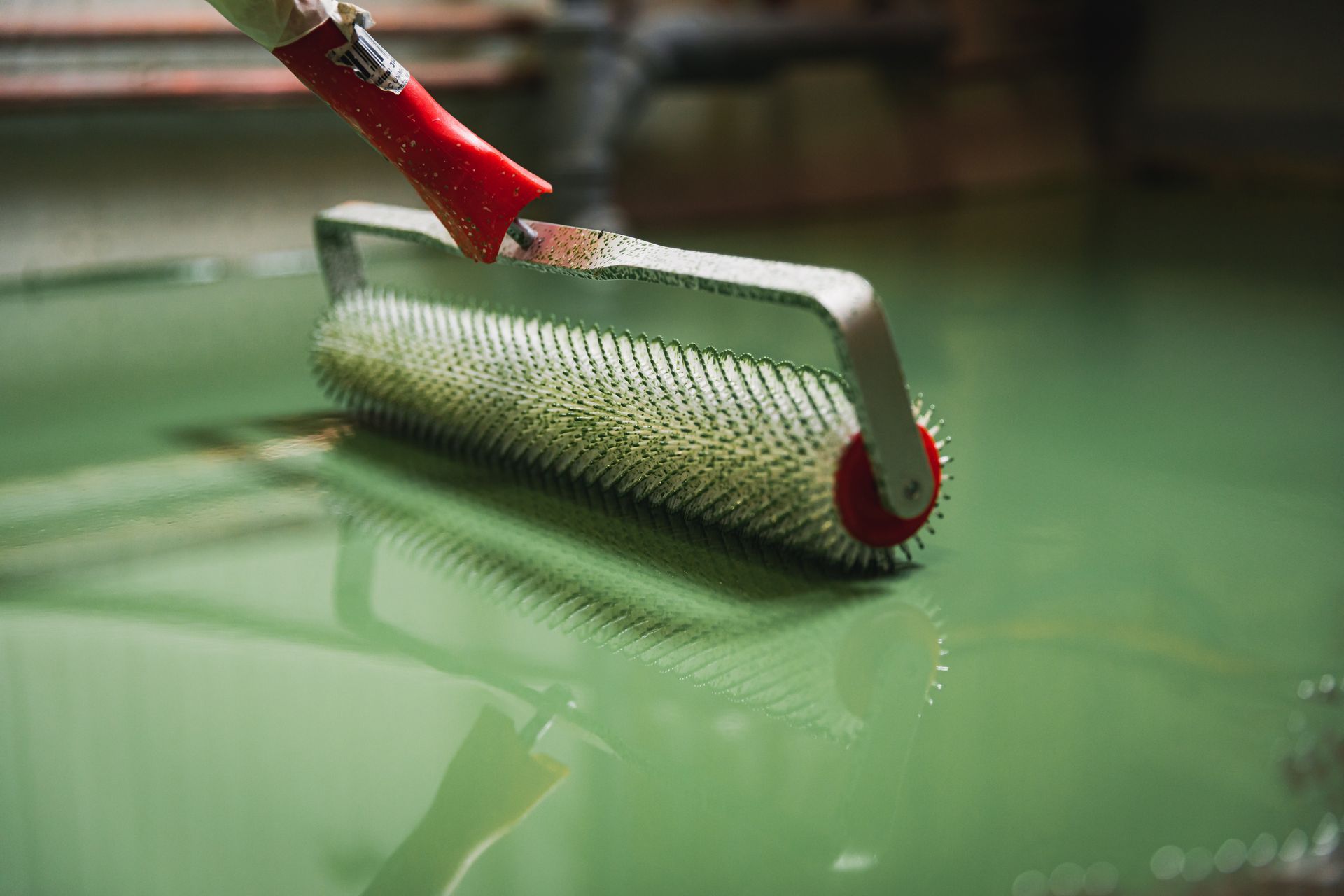 A spiky roller tool being used to smooth out green epoxy flooring.