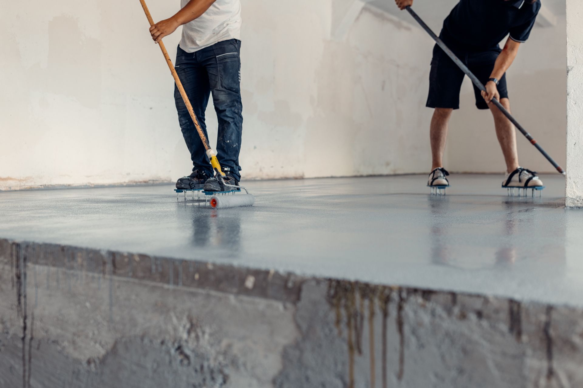 Two people applying a glossy coating to a concrete floor in a room. Two people applying a glossy coating to a concrete floor in a room.