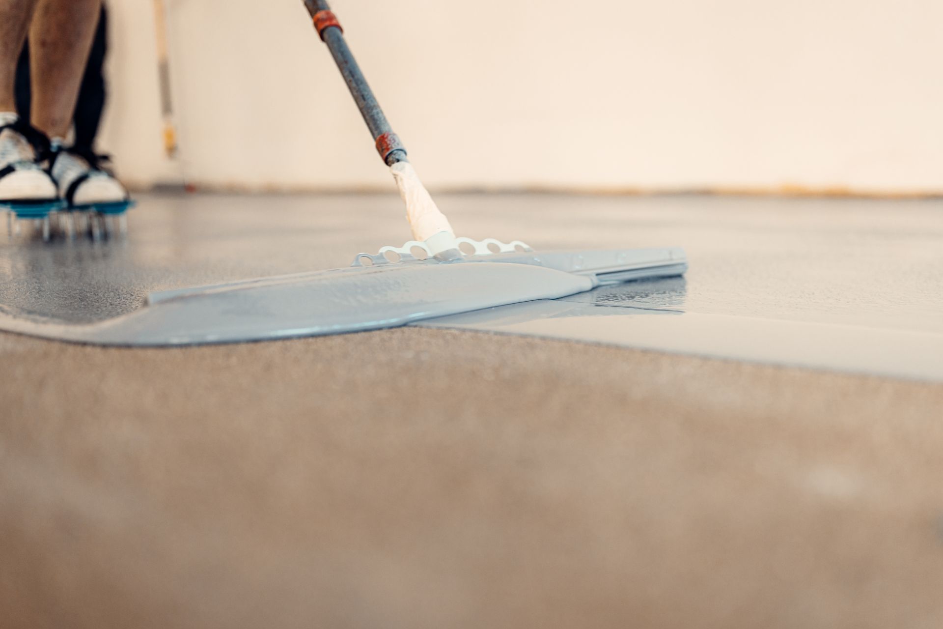Person mopping a wet, shiny, light-colored floor with a spray mop.