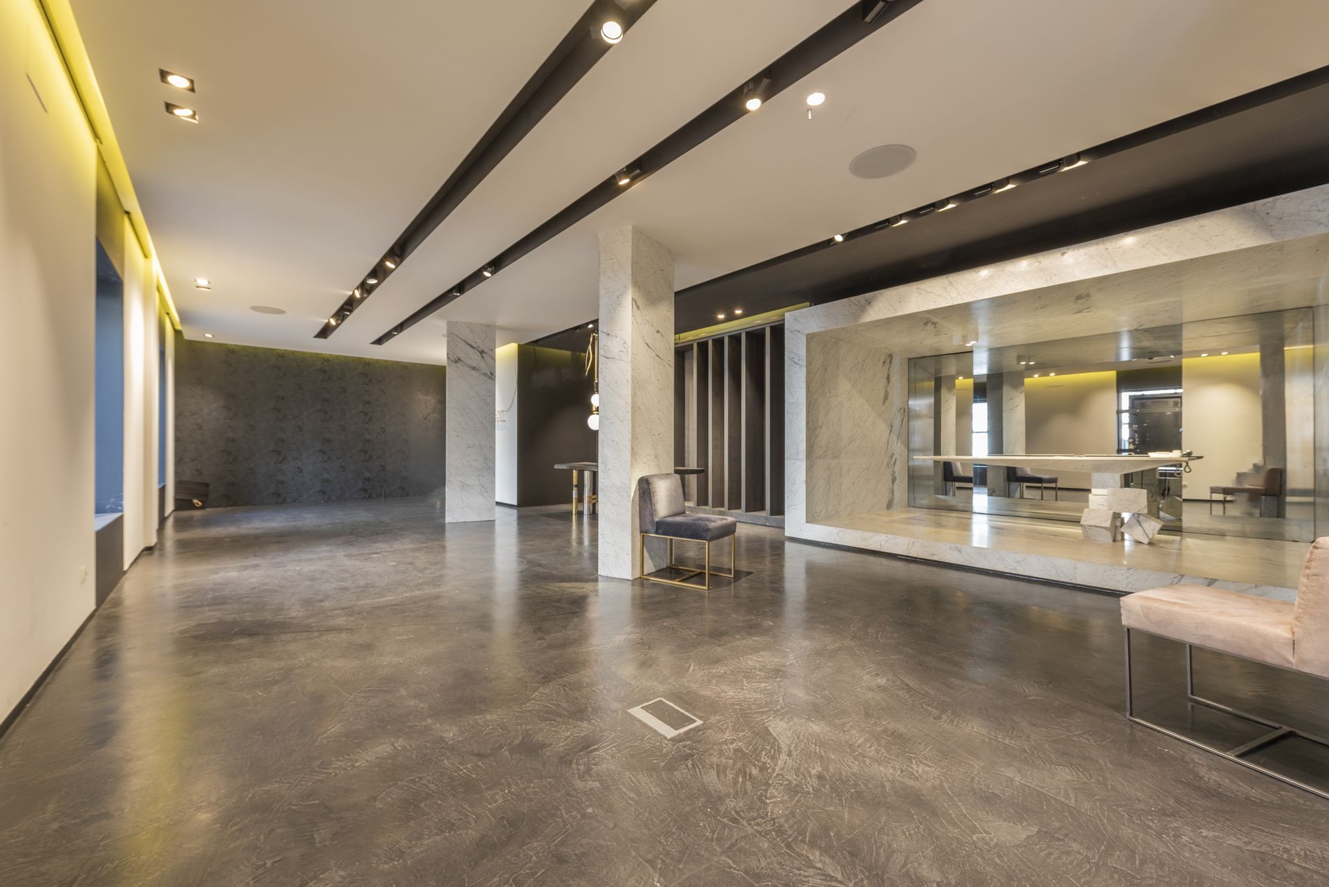 Modern, empty commercial space with polished concrete floor, track lighting, and glass-walled rooms.