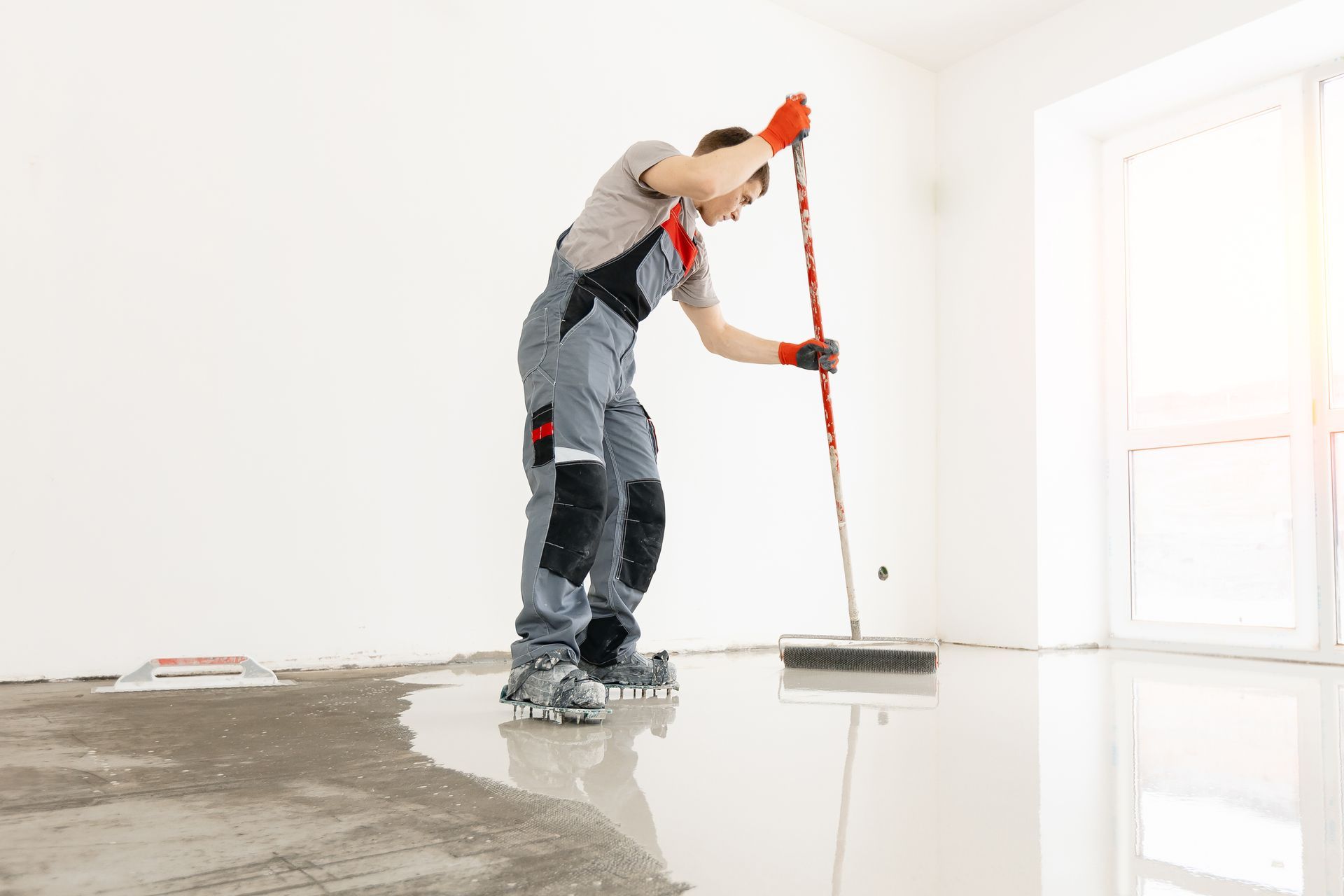 Man in overalls spreading floor sealant with a squeegee in a bright, empty room. Man in overalls spreading floor sealant with a squeegee in a bright, empty room.