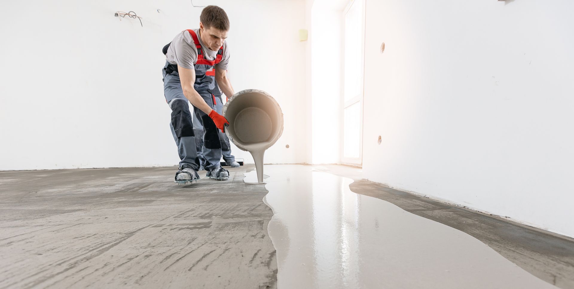 Person pouring concrete from a bucket onto a floor. Indoors, construction site, light gray concrete. Person pouring concrete from a bucket onto a floor. Indoors, construction site, light gray concrete.