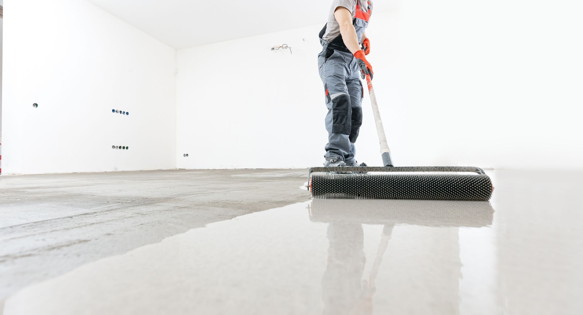 Person rolling out a concrete floor in a white room.