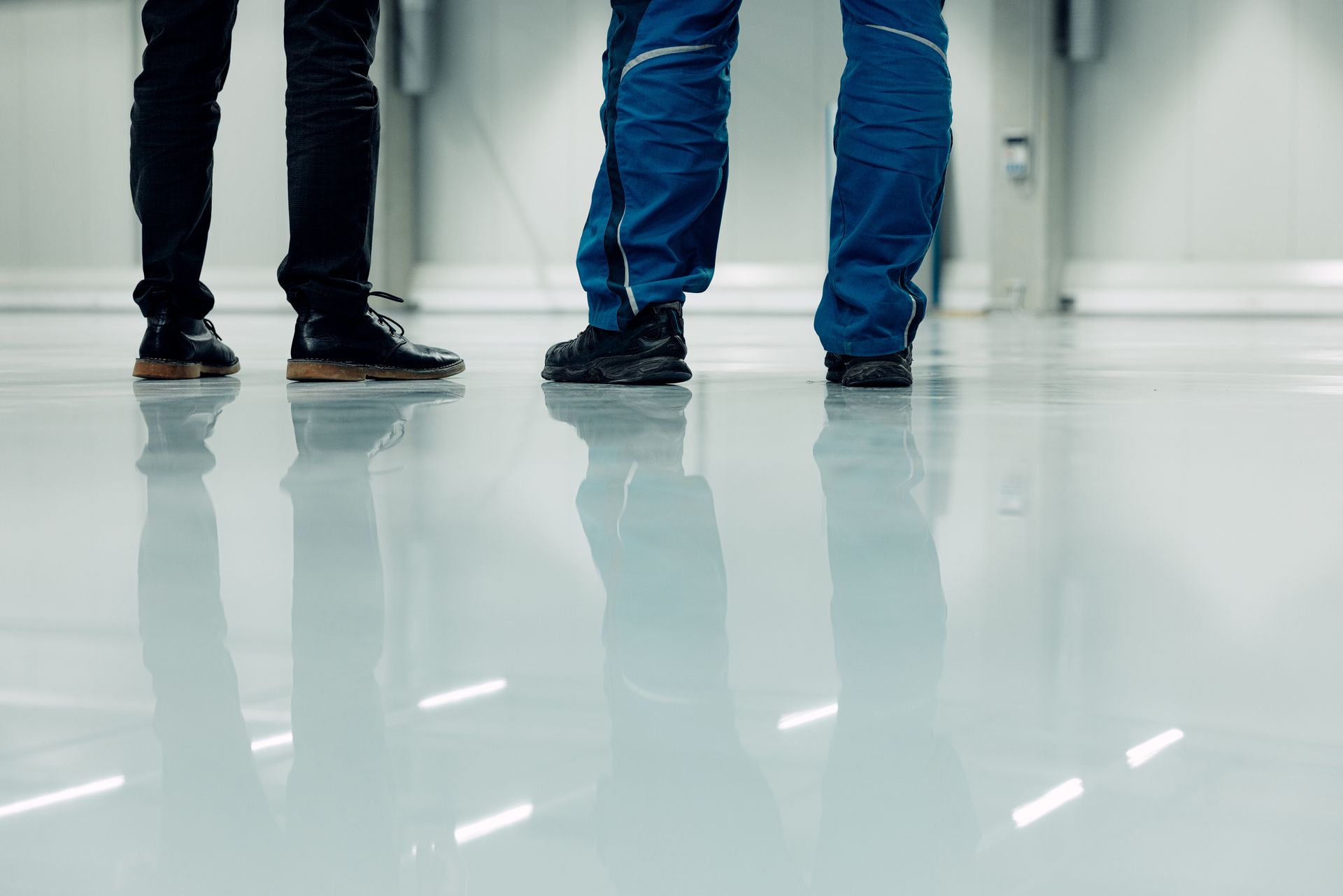 Three people's legs and shoes on a shiny, reflective floor. One person in black pants, two in blue.