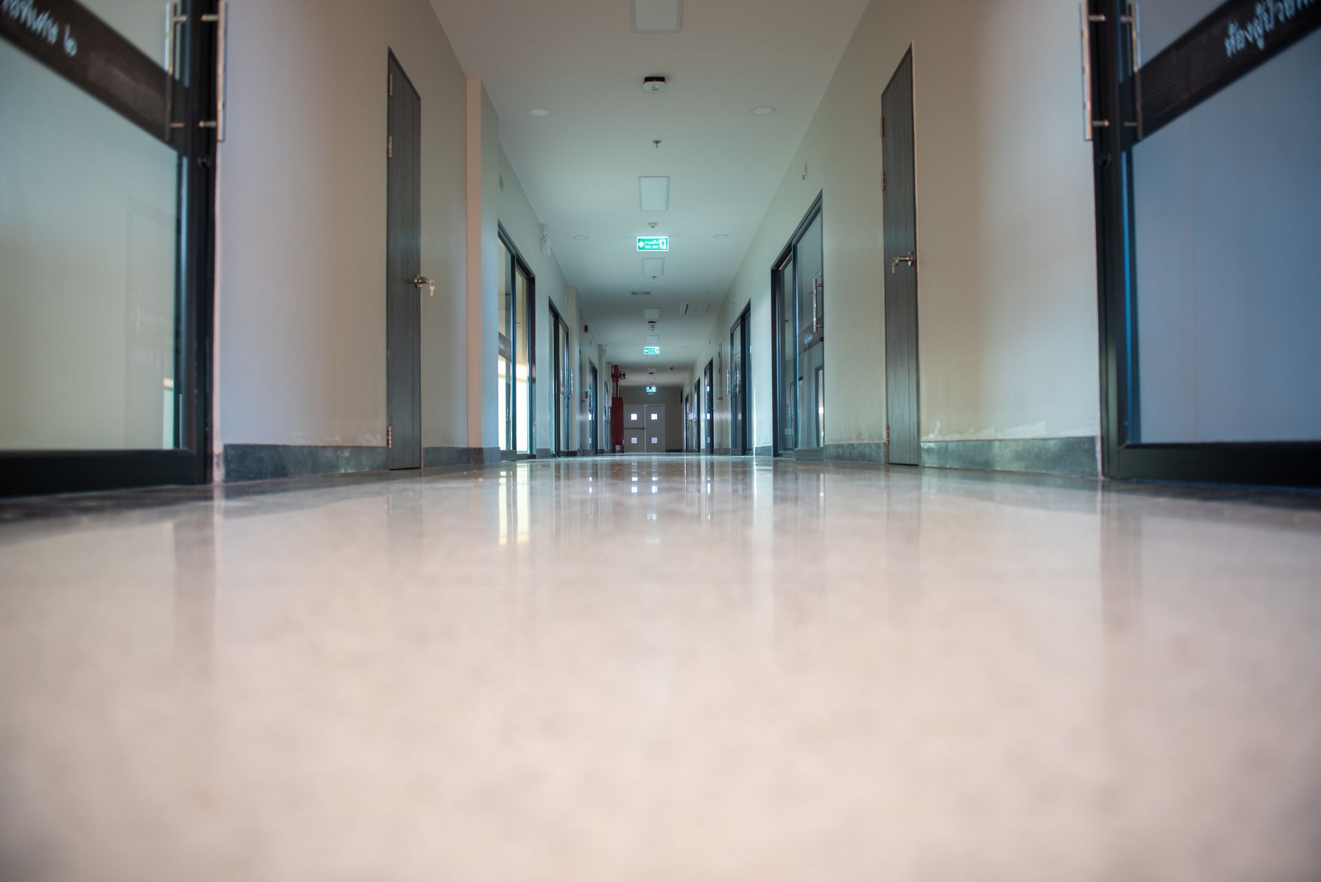 Long, brightly-lit hallway with glossy floor, doors lining both sides, perspective view.