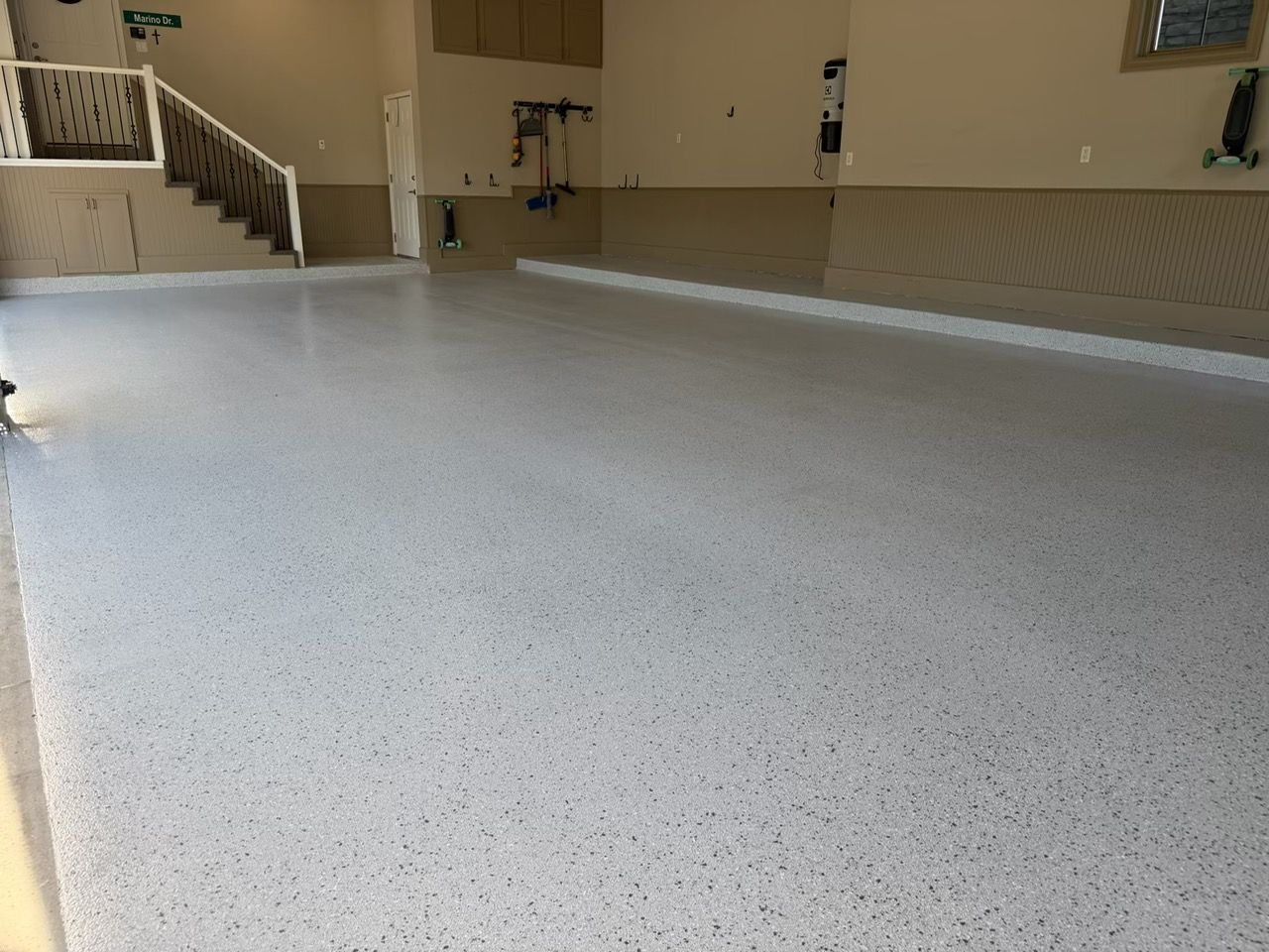 Spacious empty room with a light speckled floor, staircase, and beige walls.