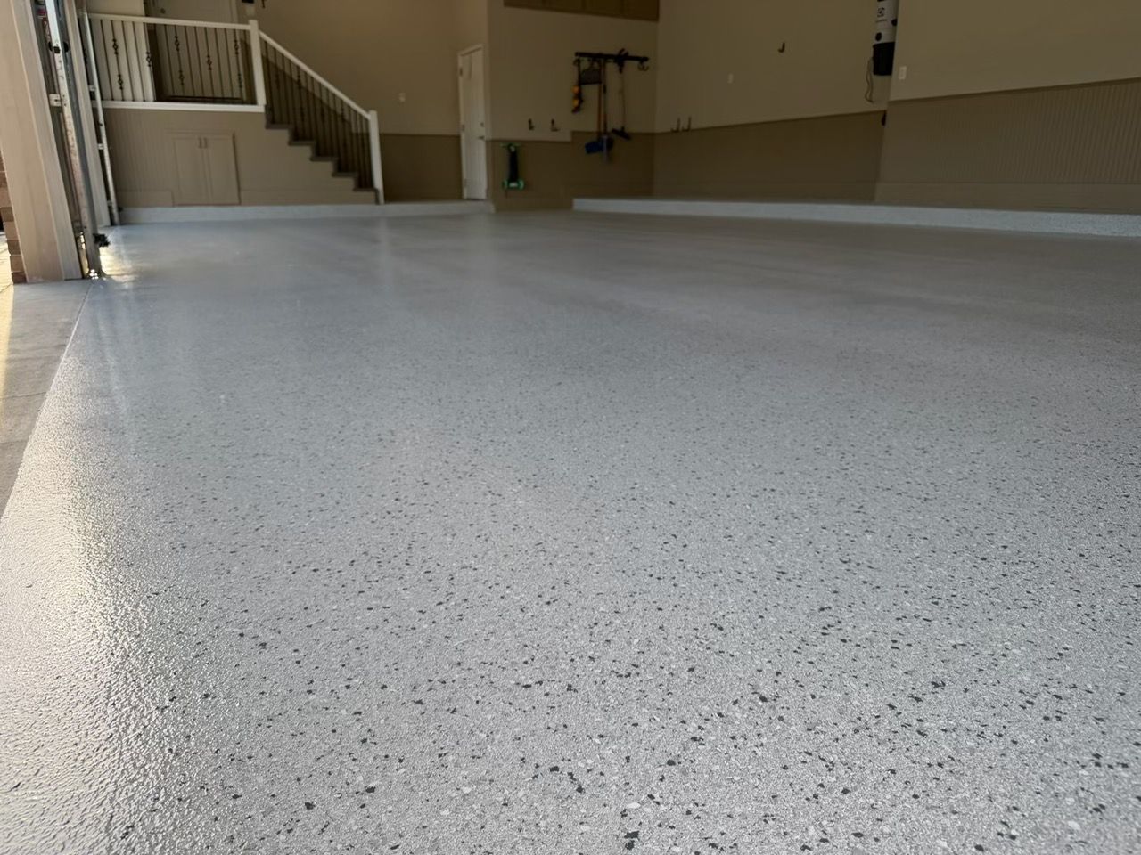 Empty indoor room with speckled white floor and staircase in the background