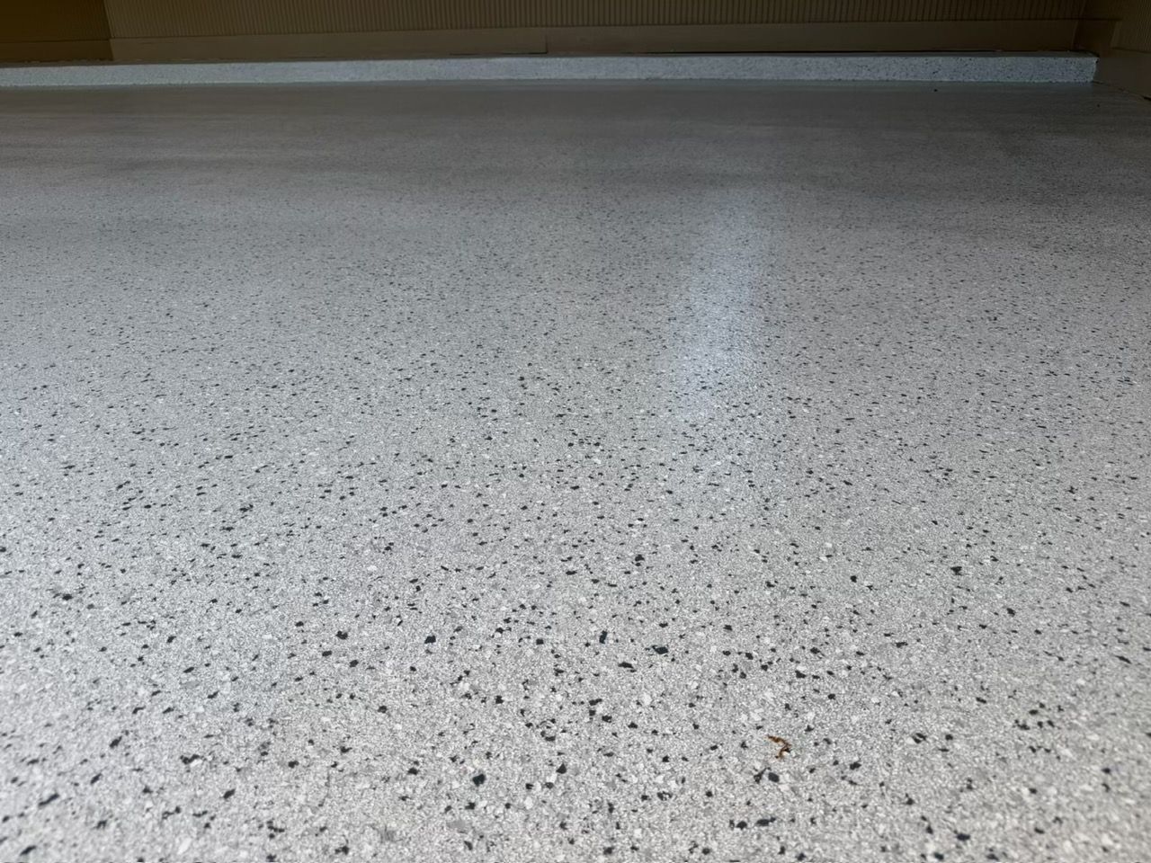 Speckled light-gray terrazzo floor with a dark baseboard in the background