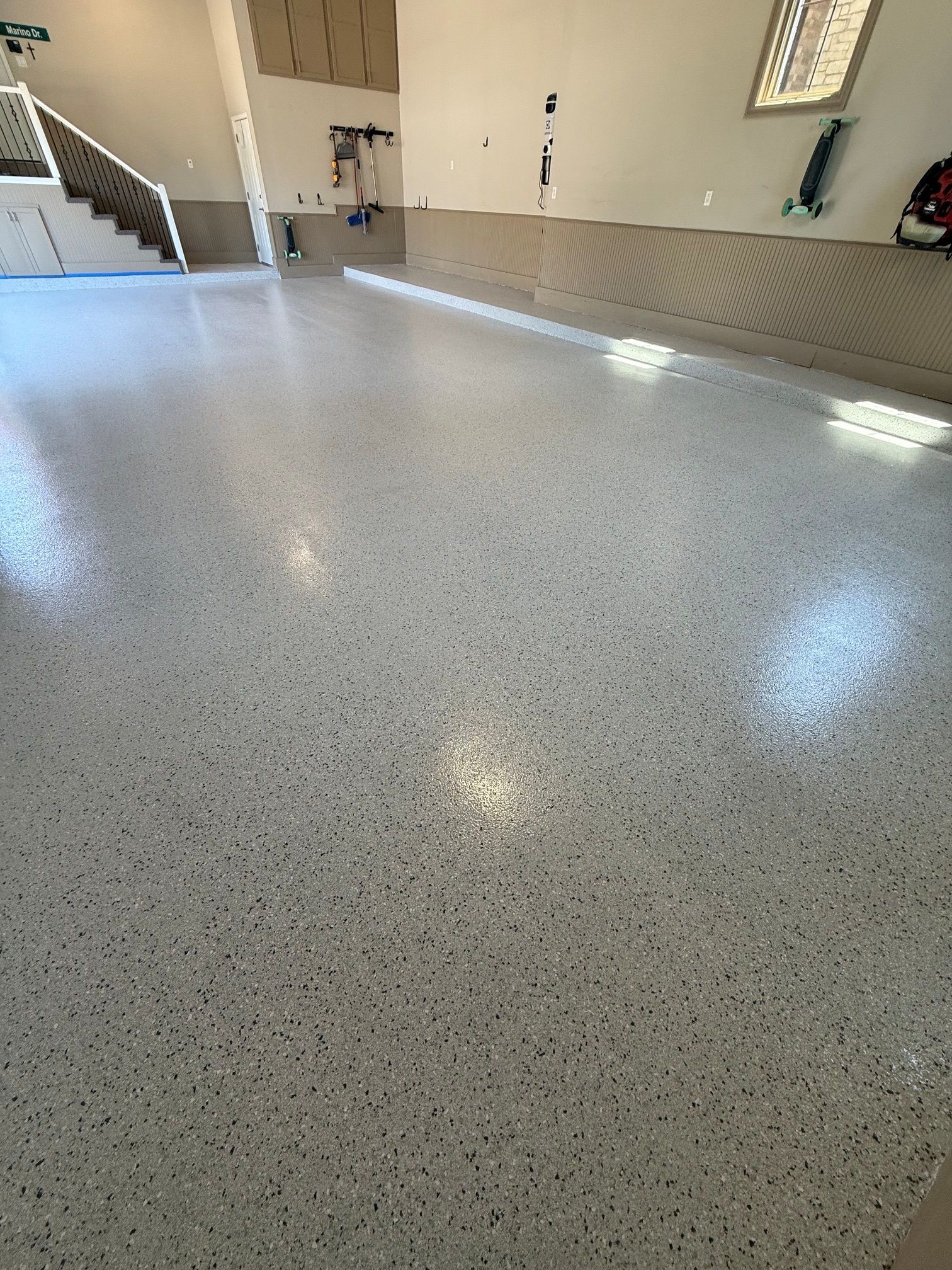 Empty speckled garage or utility room floor with windows and staircase in the background