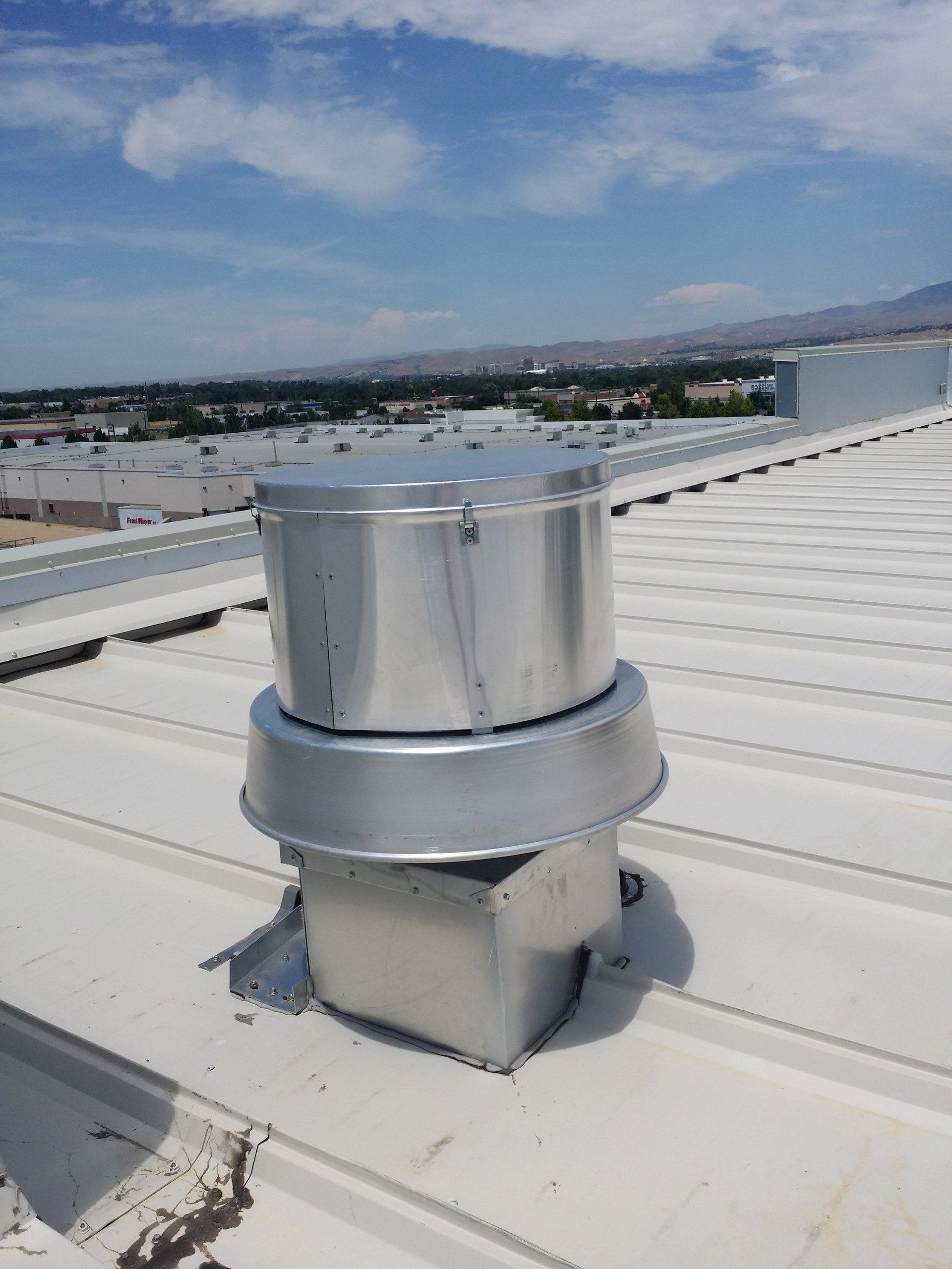 Metal roof vent on a white commercial building rooftop under a partly cloudy sky.