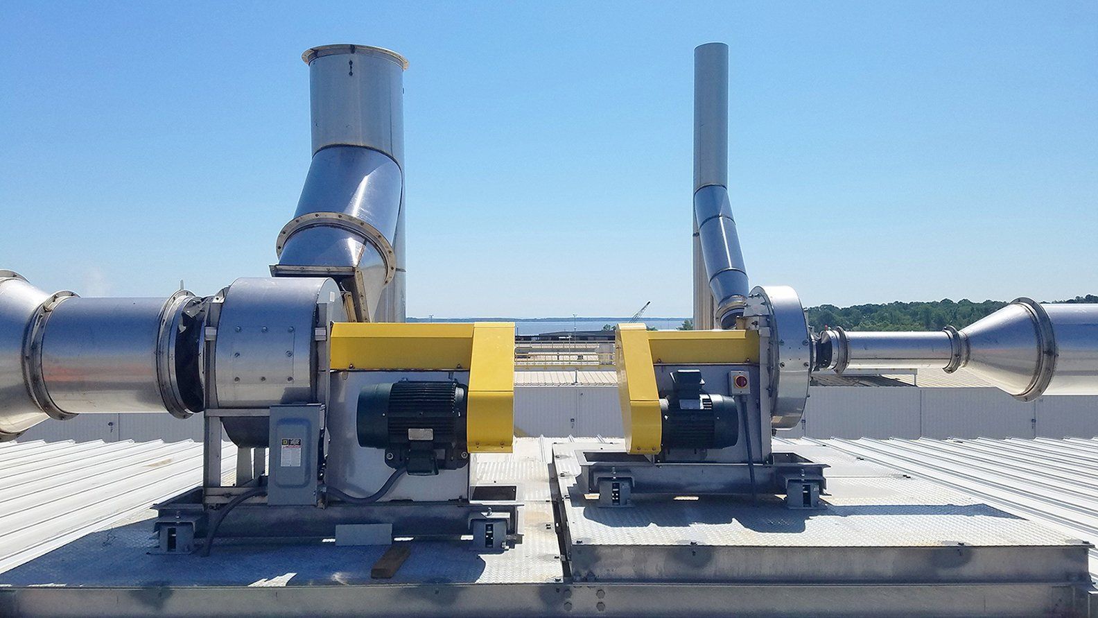 Two industrial rooftop exhaust fans with silver ducts and yellow motor covers.