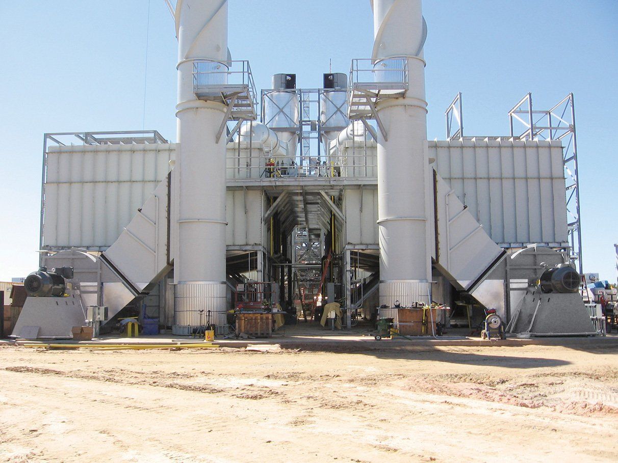 Industrial machinery with two tall exhaust stacks against a bright sky in an outdoor setting.