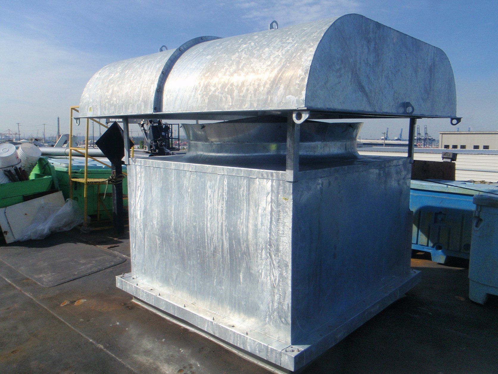 Galvanized metal industrial roof vent with curved top, on a rooftop with shipping cranes in the background.