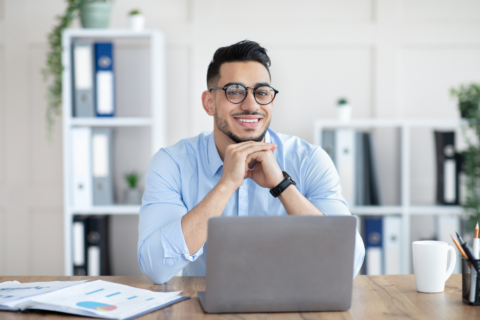 Smiling person at a desk with a laptop in a bright office