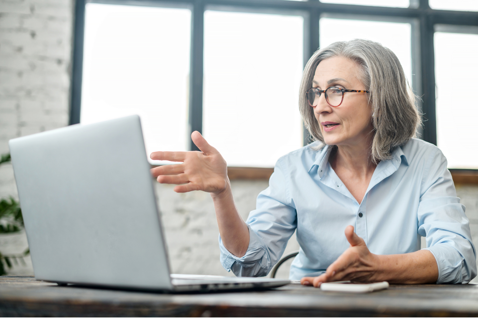 Woman speaking during a video call beside a laptop in a bright office