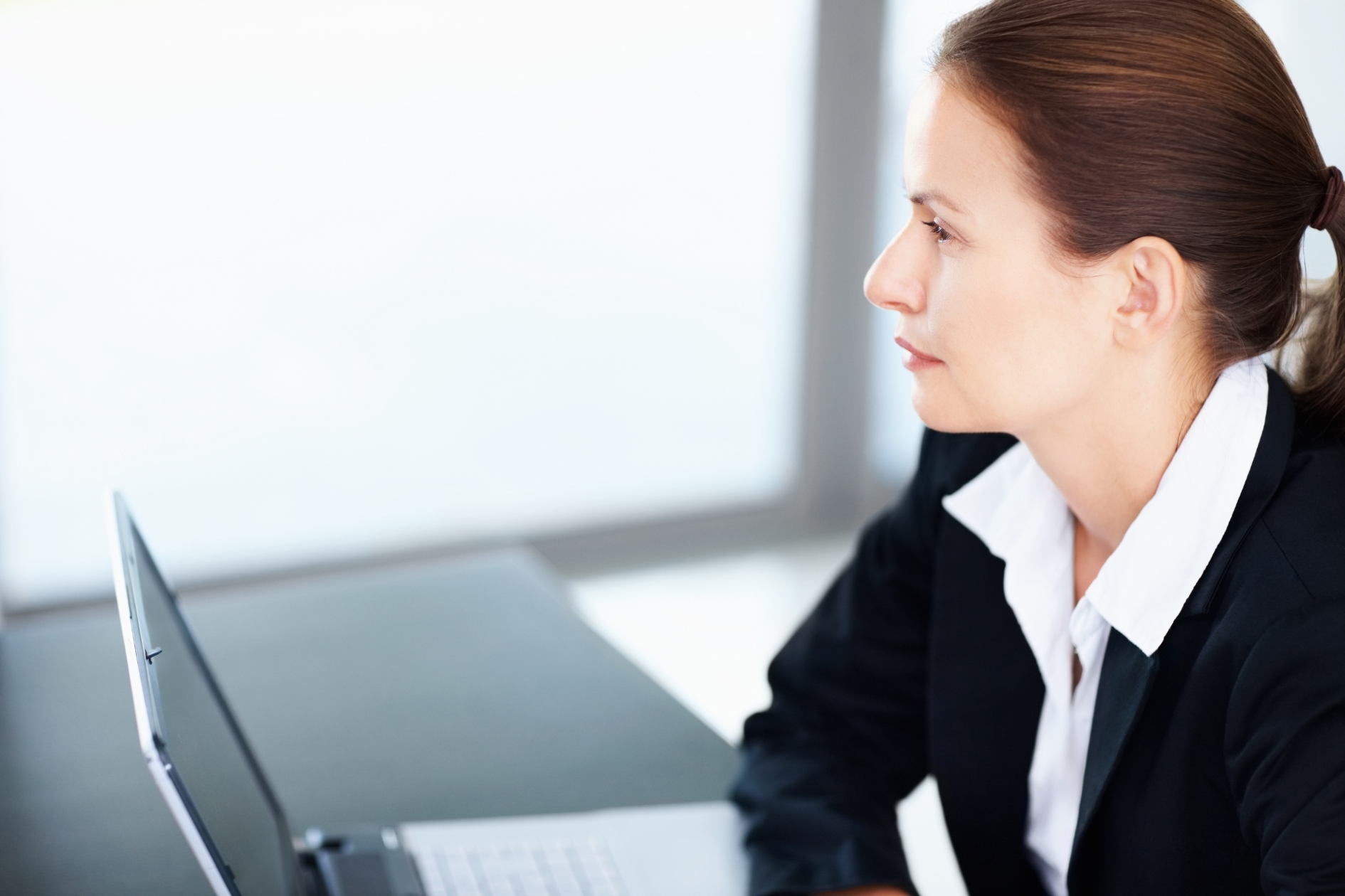 Woman in business attire working on a laptop in a bright office setting