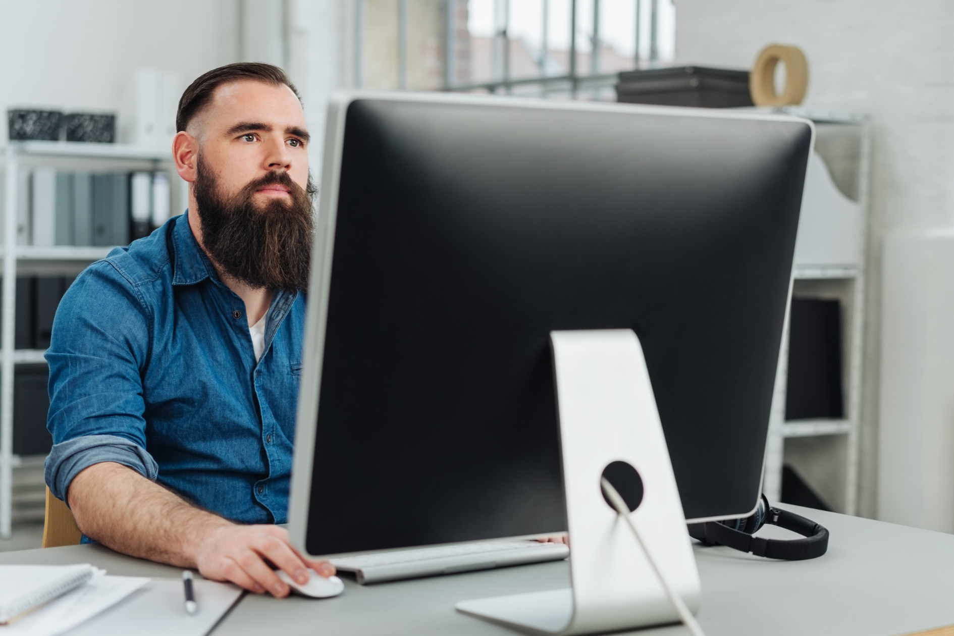 Bearded man working at a desktop computer in a bright office