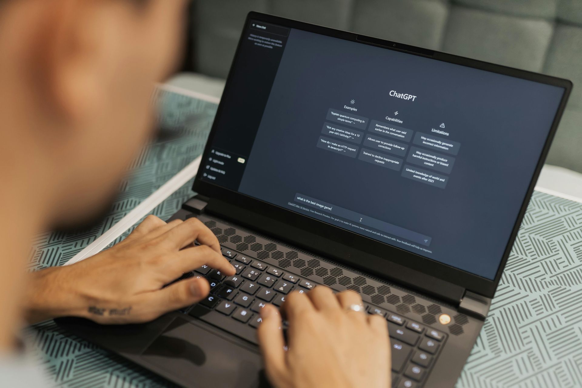 Person typing on a laptop displaying a dark settings screen with options and icons
