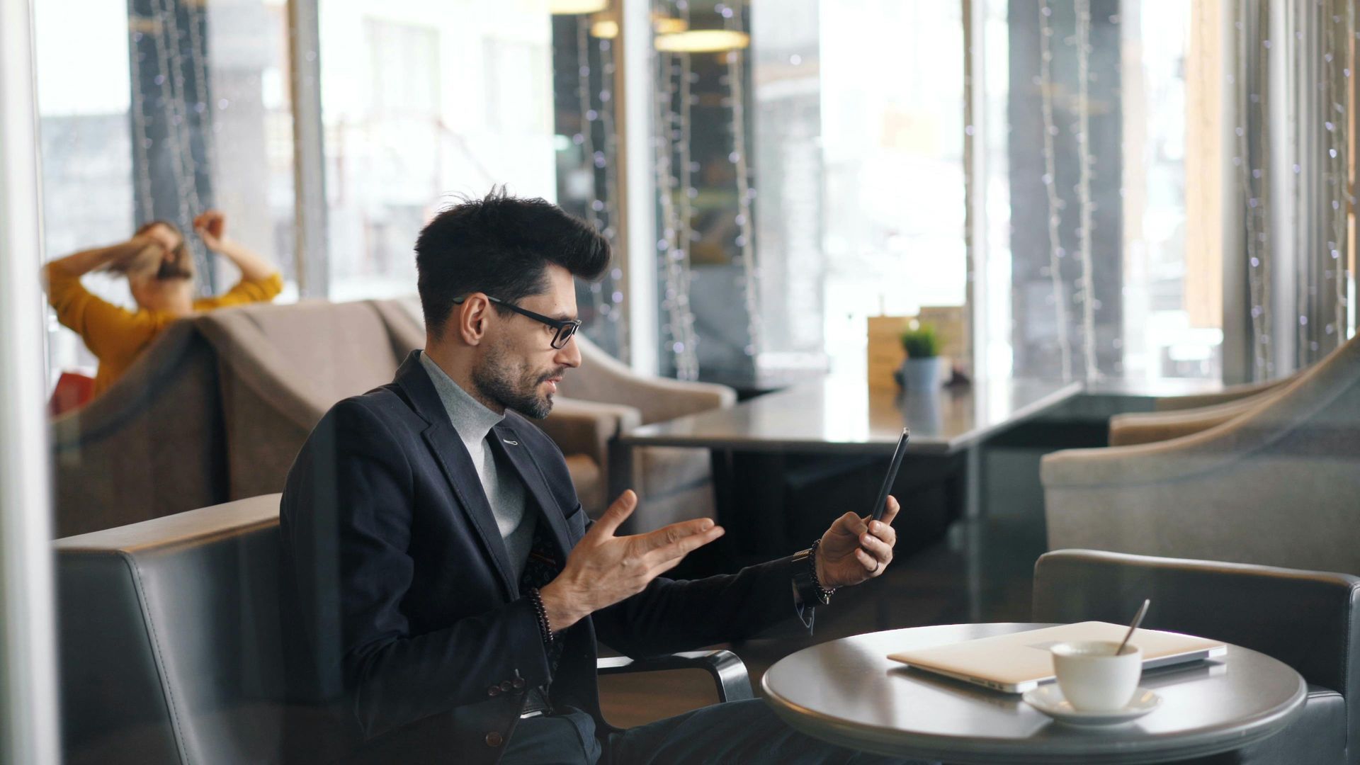 A man in a suit is sitting at a table in a restaurant using a tablet computer.