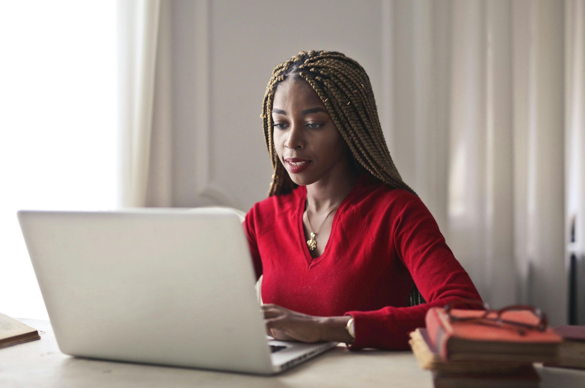 Woman in a red top working on a laptop at a desk with books nearby