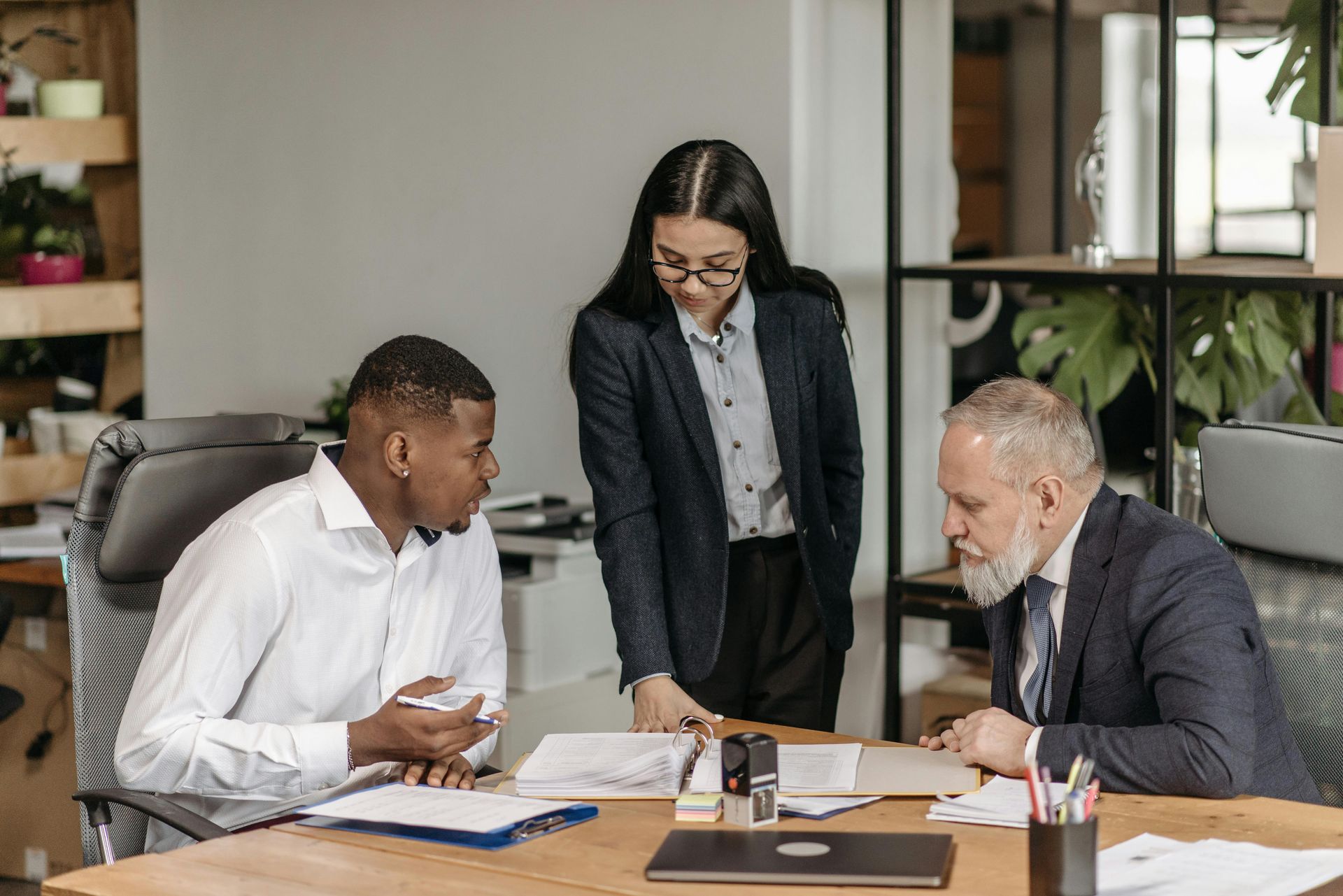 Three businesspeople, two men and a woman, reviewing documents at a desk.