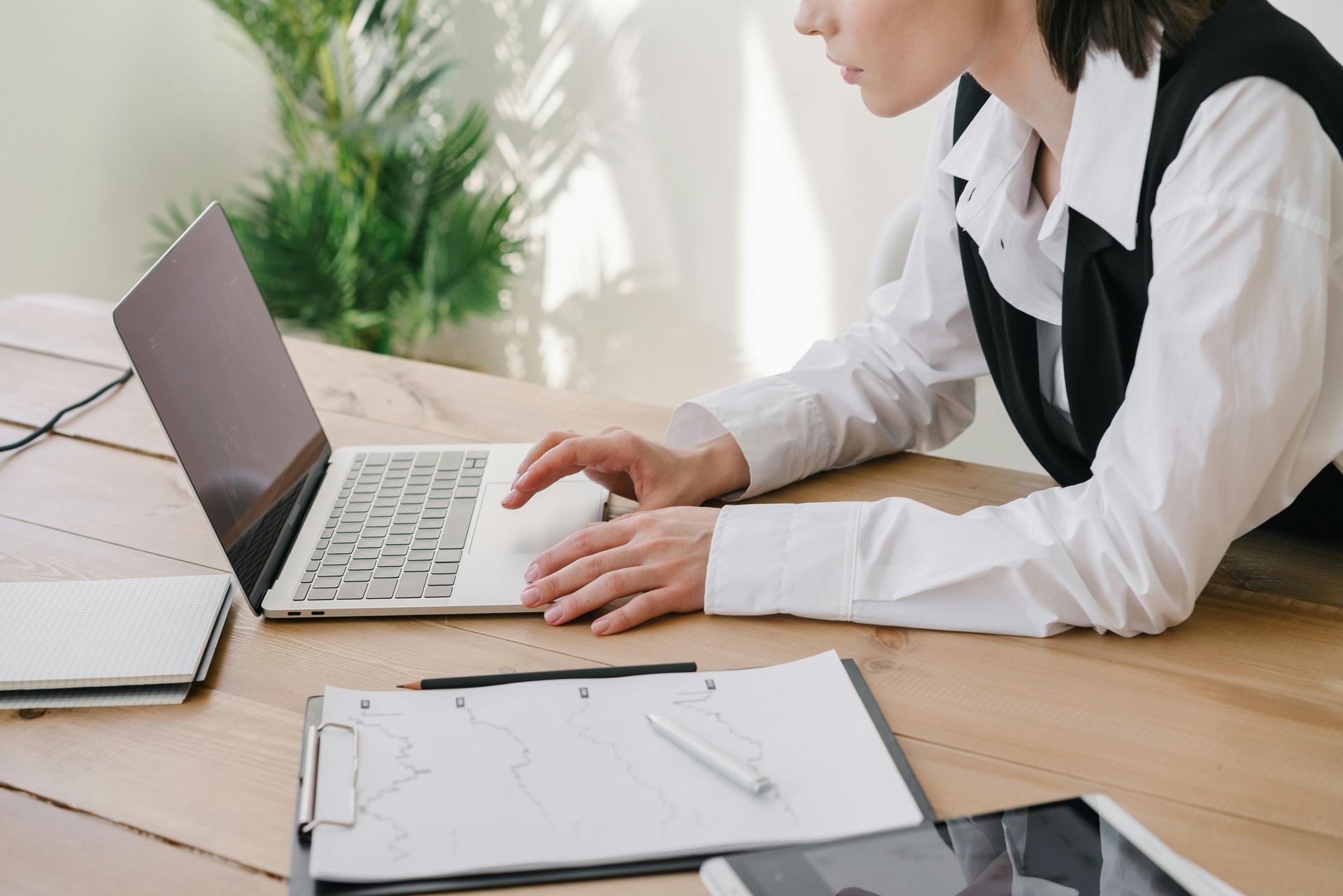 Person typing on a laptop at a desk with papers and a notebook in a bright office
